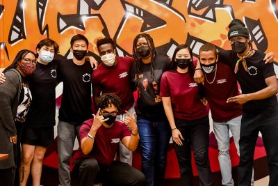 A group of students posing for a photo in front of a vibrant orange graffiti wall.