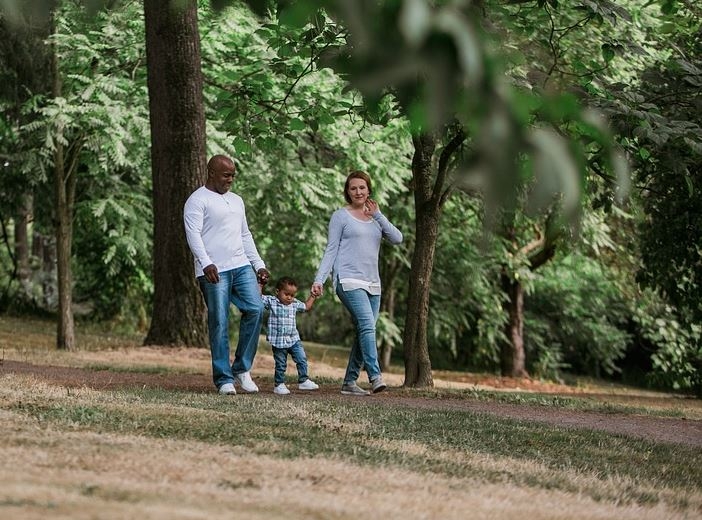 Father, young daughter and mother walking through park