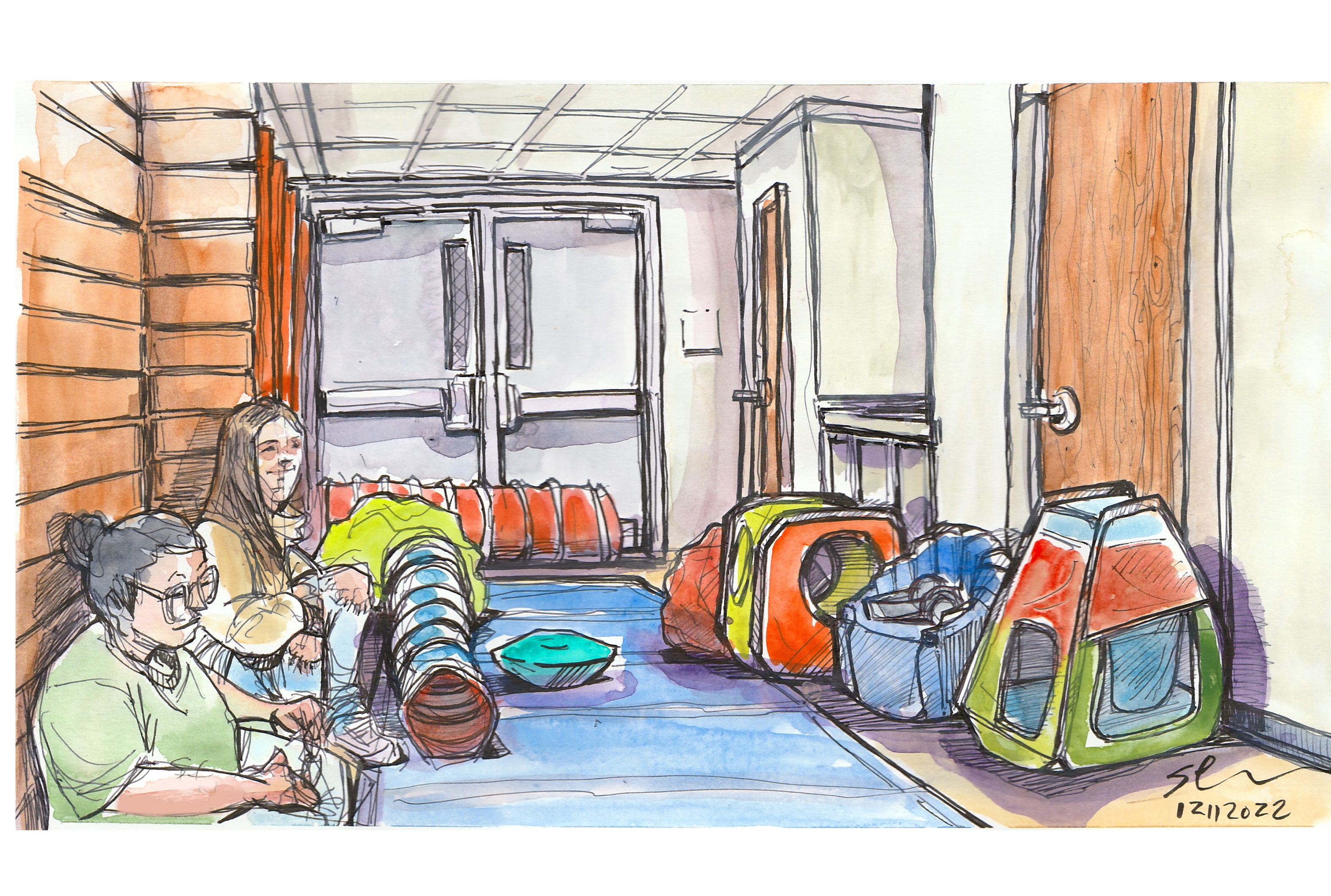 Inside the Cassell Colesium SAFE space, a small, colorful room away from the noise of the game that includes bean bags, a cushioned floor, a  play tents and other soft items. Two volunteers are sitting on the left side.